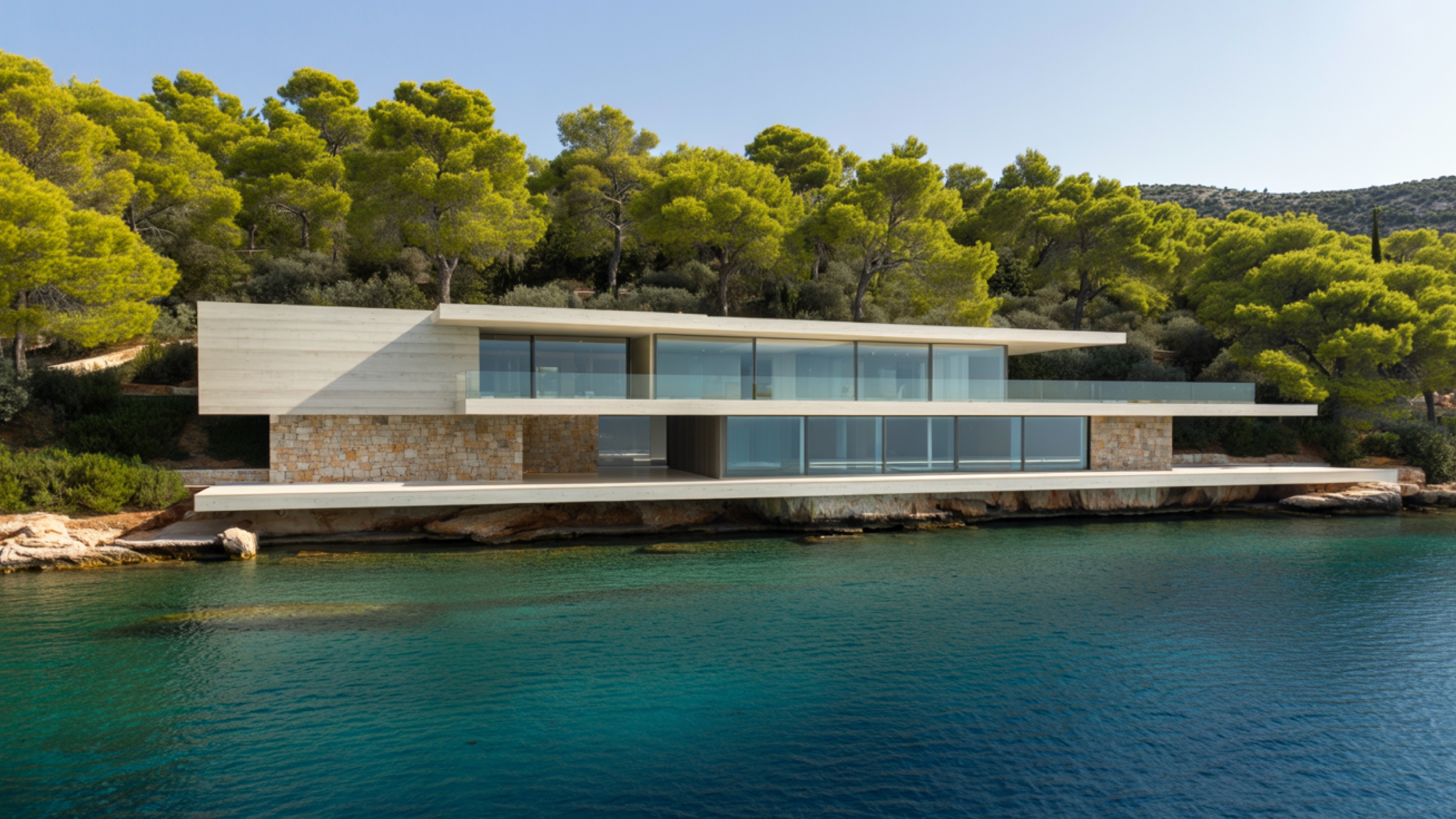 A contemporary villa of white concrete, natural stone and floor-to-ceiling glass, cantilevered over the rocks at the water's edge on the Athens Riviera. The kind of high-end coastal residence that anchors the yield curve referenced in the piece.